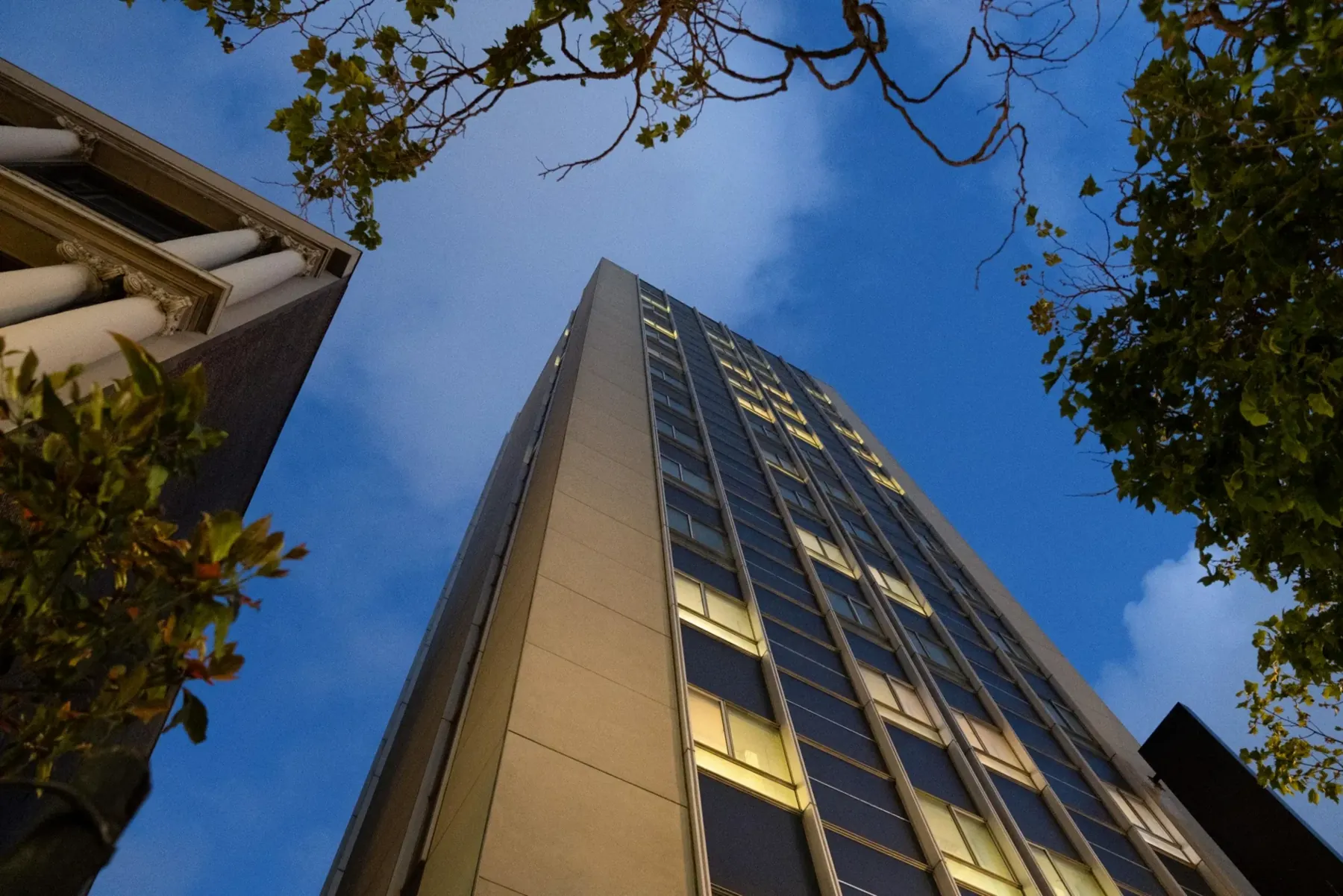 Frontier Tower in San Francisco at dusk, seen from street level with lit office windows.